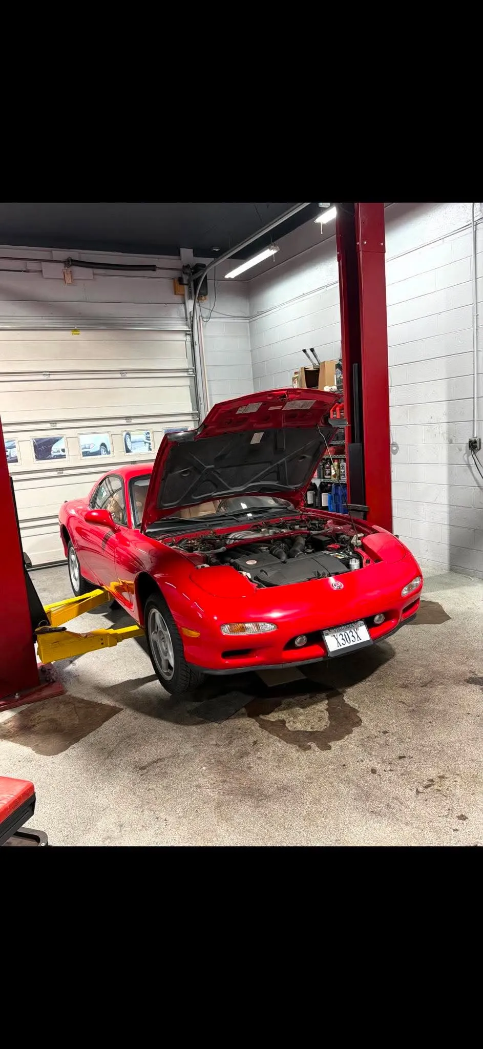 Red Mazda RX-7 Front — Front angle of a bright red Mazda RX-7 parked on a lift with the hood fully open.